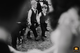 Dos adorables ringboys en traje caminando por el pasillo en Villa Medicea di Lilliano en Florencia, Toscana, sosteniendo los preciosos anillos de boda. Una hermosa fotografía en blanco y negro que captura este dulce momento.